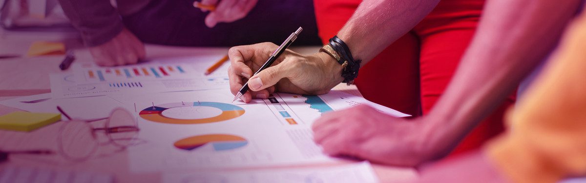 Person analysing charts and graphs with a pen on a desk, focusing on data insights.
