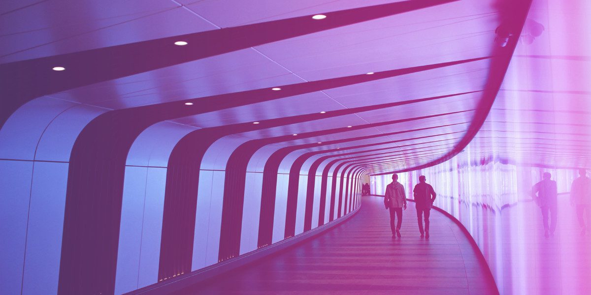 Two people walking through a futuristic, curved corridor with vibrant pink and purple lighting.