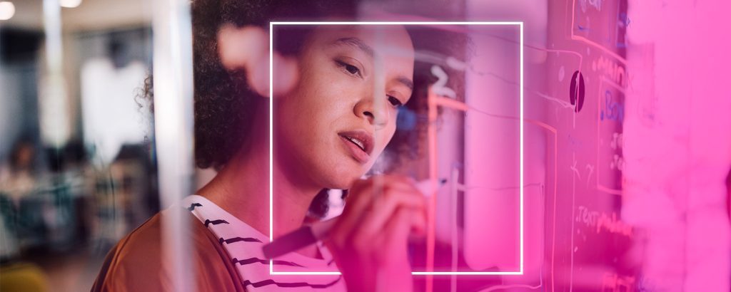Woman writing on a transparent board with focused expression, surrounded by neon pink lighting