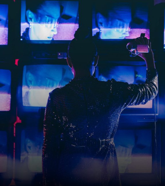 image of woman with camcorder in front of tv screens